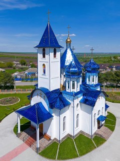 White church building with blue roofs and golden crosses in rural area, aerial view, Church of the
