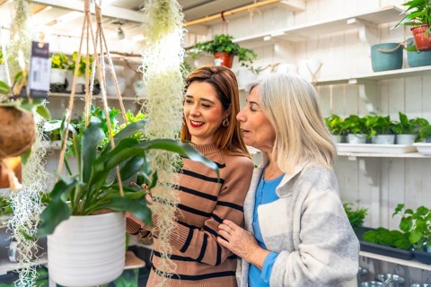 Elderly mother and adult daughter smiling while choosing potted houseplants at a bright garden