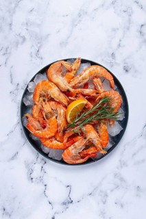 Freshly frozen shrimp on ice, with lemon and rosemary, on the marble table, top view, no people