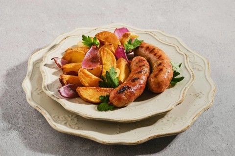 Sausages cooked on grill served with golden roasted potato wedges and purple onions on cream