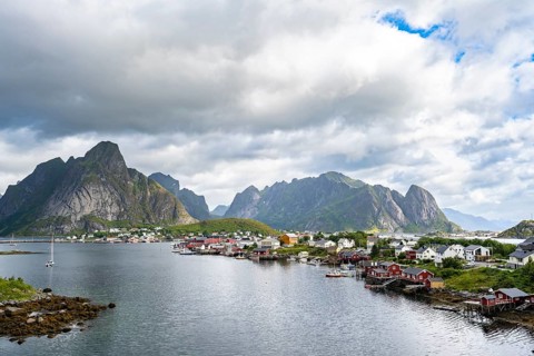 View of the village of Reine with typical red wooden houses, mountains and Reinefjord, Reine,