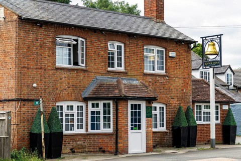 The historic former Bell pub with white porch, sash windows and topiary planters, now trading as