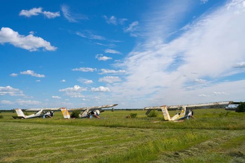 Three abandoned aircraft stand side by side on a wide field under a blue sky, PZL-104 Wilga
