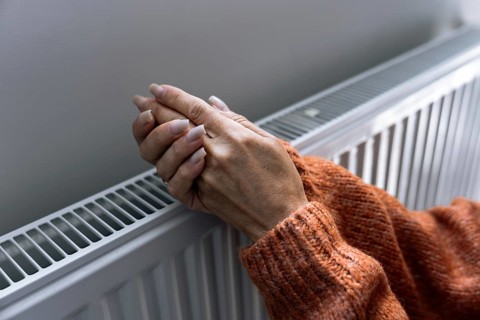 Woman warming hands near home radiator during heating season in Europe. Concept of rising utility