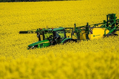 Agriculture, rapeseed field in full bloom, farmer sprays the field with a John Deere M952 trailer
