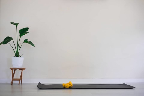 Minimalist room with a black yoga mat and yellow dumbbells beside a plant