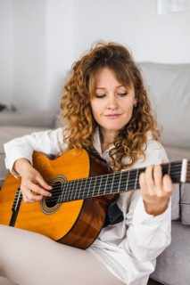 Woman with curly hair playing a guitar in a relaxed setting