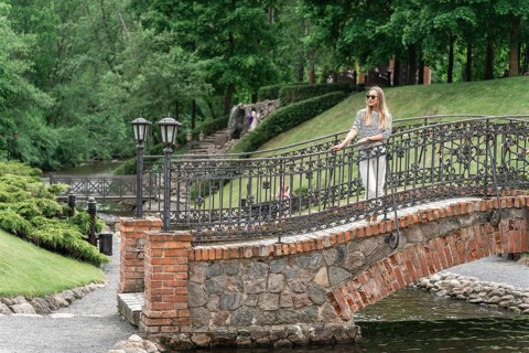 A woman stands on an old bridge in the park in the summer, Woman standing on a stone bridge with