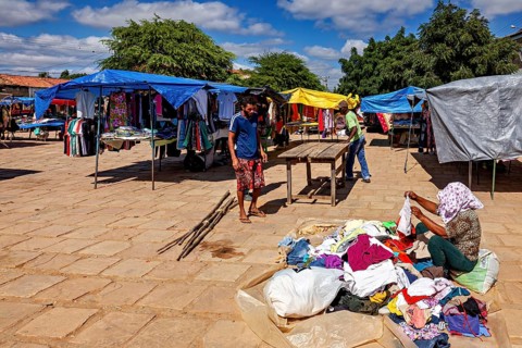 Colourful clothes spread out at a market with people inspecting goods under blue skies, market
