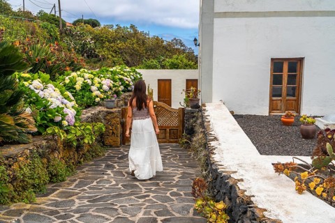 Woman in white dress exploring a beautiful traditional garden with lush hydrangeas and volcanic