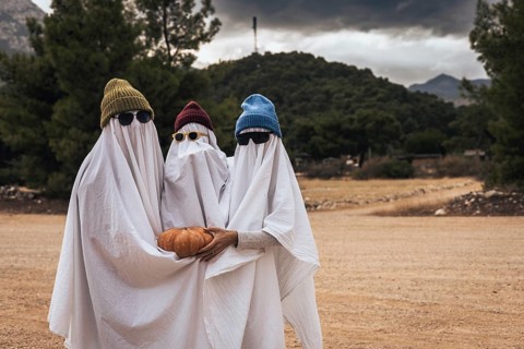 Family wearing ghost costumes and holding a pumpkin outdoors during Halloween celebration. Homemade