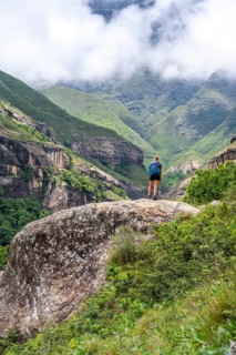 Female hiker standing in front of landscape with mountains and fog, Drakensberg National Park,
