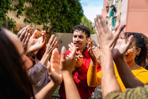 Diverse people clapping hands in a circle enthusiastically supporting and celebrating a man,