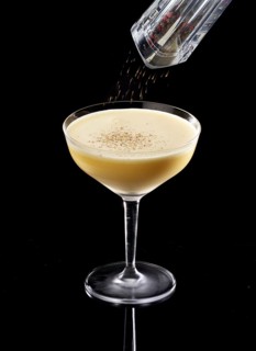 Light brown cocktail on a black background, coarsely ground pepper as garnish, studio recording