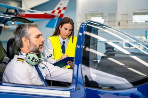 Flight instructor guiding a male pilot through pre flight checklist procedures inside a cockpit,