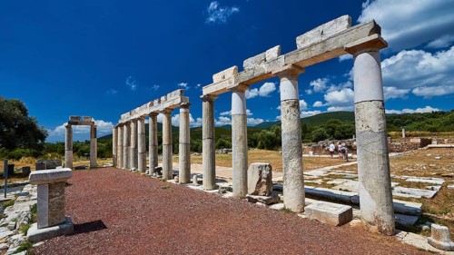 Stoa of the market, remains of ancient columns against a natural backdrop under a blue sky, ancient