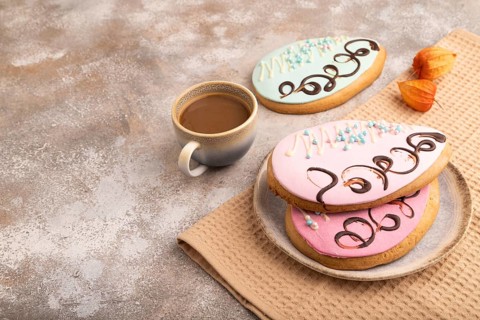 Glazed pink and blue decorated cookies, cup of coffee, on brown concrete background with linen