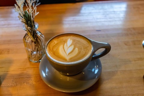 Latte art coffee cup on a wooden table, next to a small vase with decorative plants, creating a