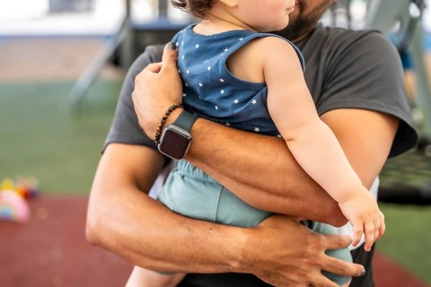 Father cradling infant outdoors at a park, tender bonding moment showing care, protection and joy