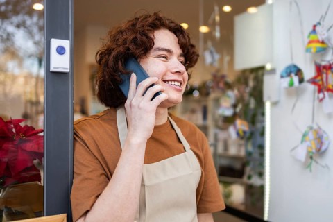 A cheerful shop owner wearing an apron stands at the organic products store entrance, smiling while