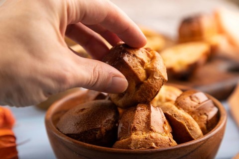 Golden caramelized Canele cookies dessert with hand, cup of coffee, on blue wooden background with