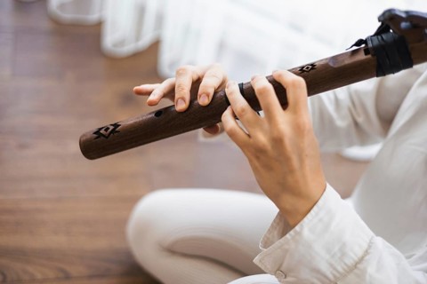 Close-up of hands playing a wooden flute with attention to musical focus