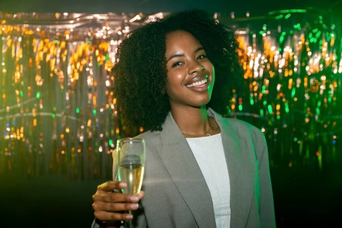 Young black woman smiling and enjoying a celebration, holding a flute of sparkling champagne with a