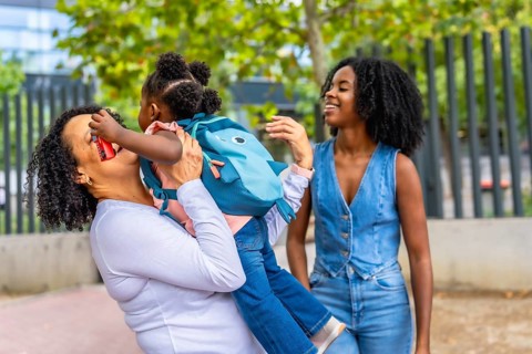 African grandmother embracing her granddaughter and laughing in a park next to her daughter