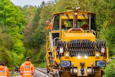 Large yellow machine on railway tracks, workers in signalling clothing, track construction Hermann
