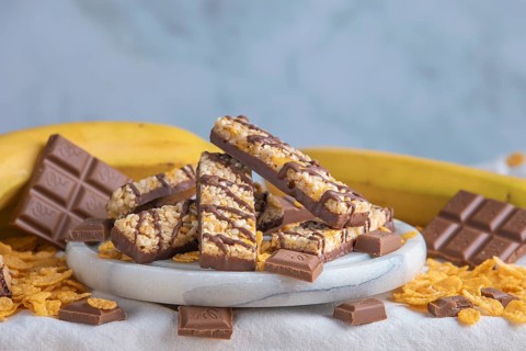 Muesli bar on a plate surrounded by chocolate, bananas and cornflakes