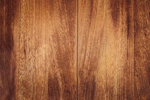 Close-up of a wooden surface with rich brown tones and visible grain patterns. The texture is