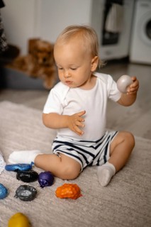 Baby in striped shorts playing with colorful toys on a rug