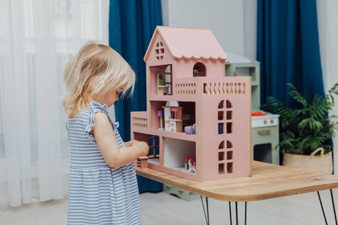 Blonde Toddler Girl playing with pink doll house in children room
