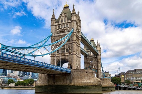Looking up at Tower Bridge from the riverside path, the ornate stonework of the tower and its