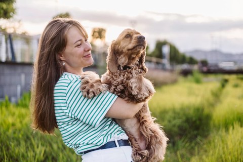 A woman affectionately holding her dog Cocker Spaniel in a park during the evening