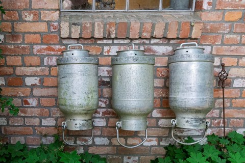 Three old milk cans hang in front of a brick wall that gives off a rustic atmosphere, North