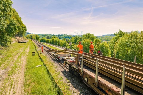 Railway workers working on a railroad car, surrounded by green landscape and blue sky, construction