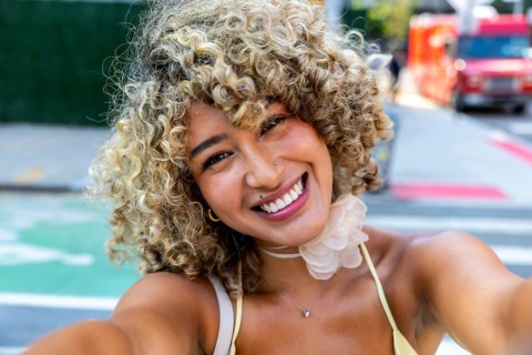 Young diverse woman with curly blonde hair smiling broadly at the camera, capturing a moment of joy