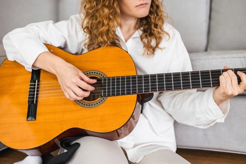 Close-up of a woman playing an acoustic guitar, focusing on her hands and the strings