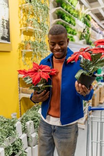 A person stands in a home goods store during the afternoon and arranges a red flower pot on a shelf