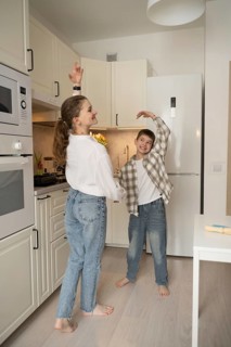 A joyful mother and son share a playful dance in a bright kitchen, creating a warm, heartfelt