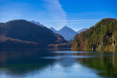 Idyllic mountain lake with clear reflection of the green slopes under a blue sky, Schwansee, copper