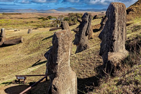Stone figures stand on a hill with a wide view of the countryside and blue sky, The Moai Statues on