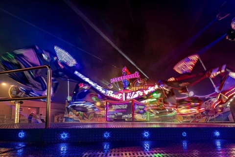 An illuminated carousel in full motion at night, surrounded by colorful lights at a fair, carousel