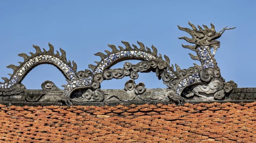 Traditional dragon figure on a roof, decorated with ceramic tiles, under a blue sky, dragon figure