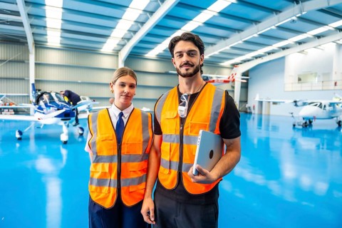 Aviation professionals wearing safety vests and standing confidently in an airplane hangar with