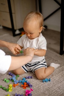 A toddler is aided by an adult while playing with colorful toys, capturing a moment of guidance