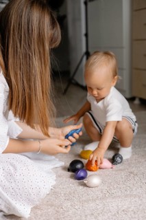 A mother interacts with a toddler playing with colorful toys on the floor, highlighting learning