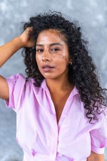 Vertical close-up portrait against a grey urban wall of a sensual latin woman posing holding her