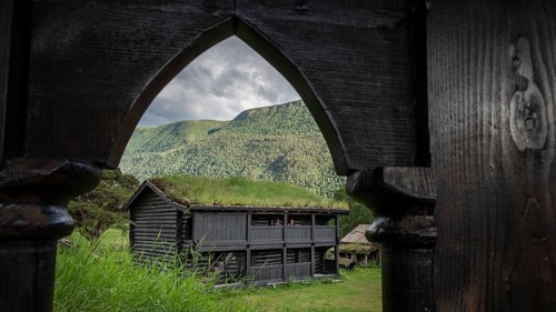 View through a wooden archway, traditional wooden house with grass sod roof in front of a cloudy